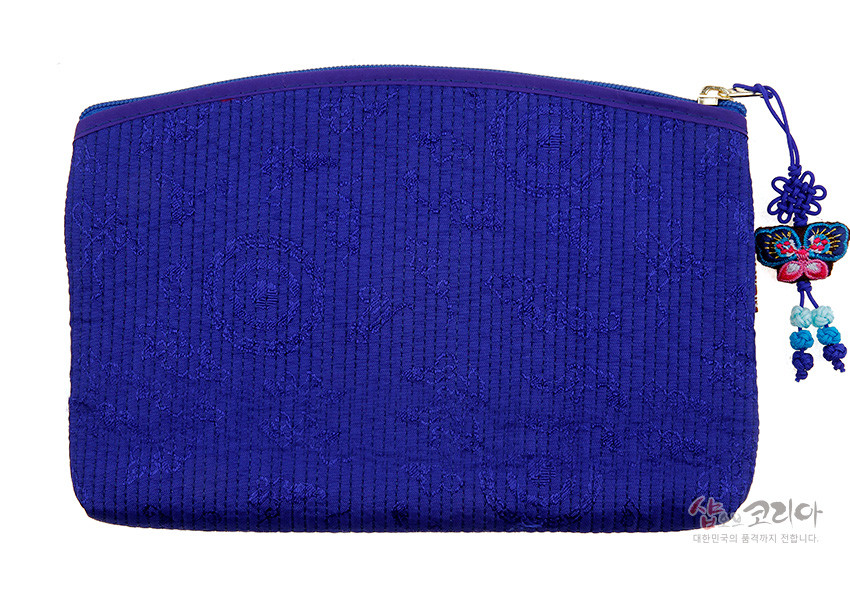 [텍스트: 샵오브코리아 대한민국의 품격까지 전합니다.] 진한 청색 누비 원단에 세로줄 퀼팅과 전통 문양이 더해진 직사각 지갑, 지퍼에 나비 모양 자수 매듭 장식이 달린 디자인