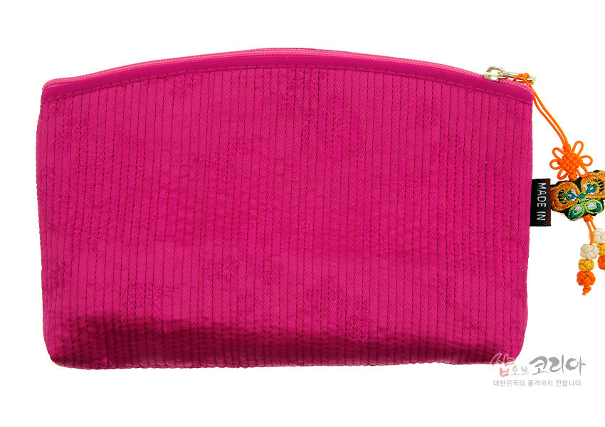 [텍스트: MADE IN, 샵오브코리아 대한민국의 품격까지 전합니다.] 진분홍 색상의 세로 누비질 원단과 금속 지퍼, 전통 노리개 매듭 장식이 어우러진 직사각형 티슈 지갑 모습