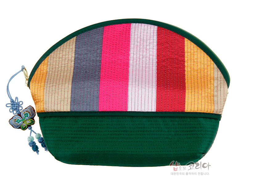 [텍스트: 샵오브코리아 대한민국의 품격까지 전합니다] 녹색 바탕에 분홍·빨강·회색 등 세로 색동 비단 누비 기법이 더해진 반원형 파우치와 나비 자수 매듭 장식 디테일