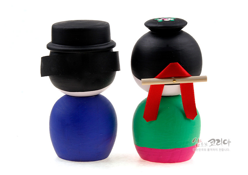 [텍스트: 샵오브코리아 대한민국의 품격까지 전합니다.] 원목 재질에 아크릴 채색으로 표현한 전통 혼례 신랑신부 뒷모습 목각 인형, 원색 한복과 족두리·댕기 장식이 특징인 디자인