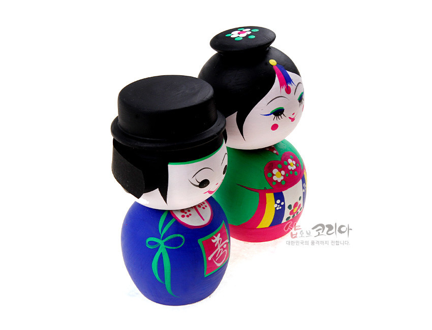 [텍스트: 샵오브코리아 대한민국의 품격까지 전합니다.] 원목에 아크릴 채색으로 표현한 전통 혼례 신랑신부 목각 흔들인형, 원색 한복과 꽃·수복 문자 문양 장식 특징