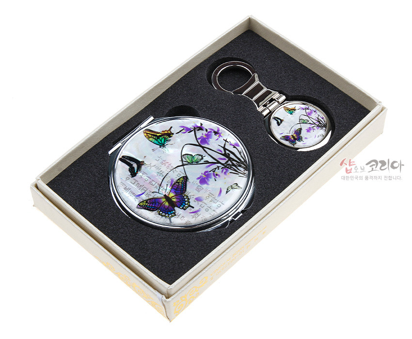 [텍스트: 샵오브코리아 대한민국의 품격까지 전합니다.] 자개 상감 기법 위 난초와 나비 문양, 오팔빛 채색이 돋보이는 금속 테두리 손거울·열쇠고리 세트 이미지