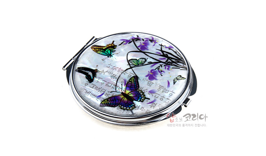 [텍스트: 샵오브코리아 대한민국의 문화까지 전합니다.] 자개 바탕 위에 옻칠 기법으로 표현한 보랏빛 난초와 오색 나비 문양, 금속 테두리가 어우러진 손거울 디자인