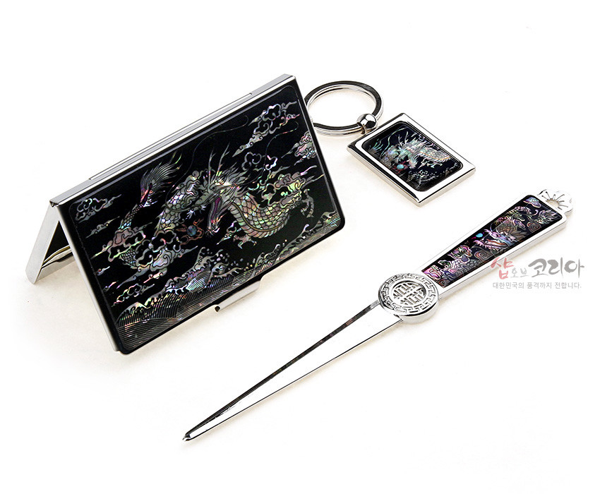 [텍스트: 샵오브코리아 대한민국의 혼과 멋까지 전합니다.] 검은 바탕 금속 위 오색 자개 상감으로 용과 구름 문양을 넣은 명함집, 열쇠고리, 지칼 3종 세트 구성