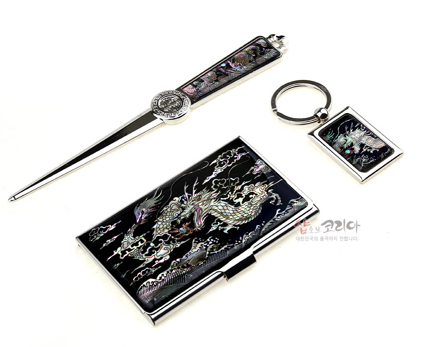 [텍스트: 샵오브코리아 대한민국의 품격까지 전합니다.] 검은 바탕 금속 위 자개 상감 기법으로 오색 용과 구름 문양을 넣은 명함집, 책갈피, 열쇠고리 3종 세트 이미지 설명