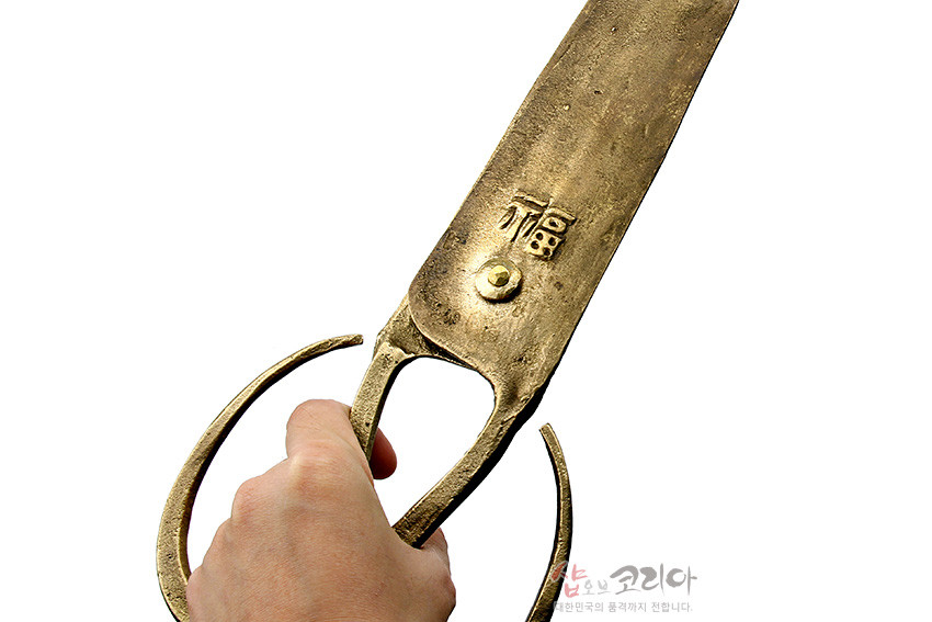 [텍스트: 복] 황동빛 금속 재질의 전통 엿가위, 거친 질감과 넓은 날, 곡선형 손잡이와 상단에 새겨진 복자 음각 문양이 돋보이는 디자인