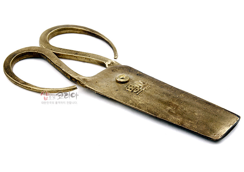 [텍스트: 샵오브코리아 대한민국의 품격까지 전합니다.] 황동빛 금속 재질의 전통 엿가위, 투박한 질감과 넓은 날, 곡선형 이중 고리 손잡이, 몸체에 새겨진 한자 음각 문양이 돋보이는 공예품