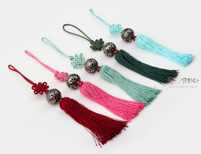[텍스트: 샵오브코리아, 대한민국의 품격까지 전합니다.] 상감 기법의 금속 원형 구슬과 전통 매듭, 비단 실타래 술이 조화를 이룬 오방색 계열 작은 노리개 장식