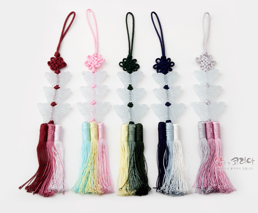 [텍스트: 샵오브코리아 한국의 품격까지 전합니다.] 반투명 유리 느낌의 나비 문양 장식 3개와 오방색 계열 비단 매듭, 삼단 그라데이션 술이 어우러진 전통 노리개 장식