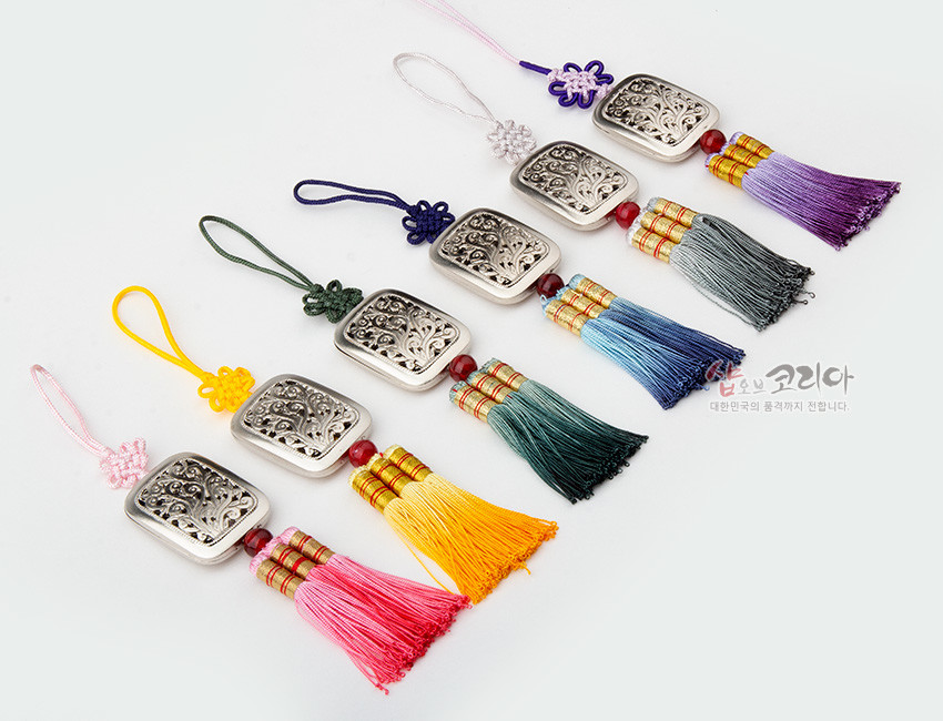 [텍스트: 샵오브코리아 대한민국의 품격까지 전합니다.] 은색 금속 사각 장식에 투각된 식물 문양, 오색 전통 매듭 끈과 그러데이션 실 술이 조화를 이룬 작은 노리개 디자인