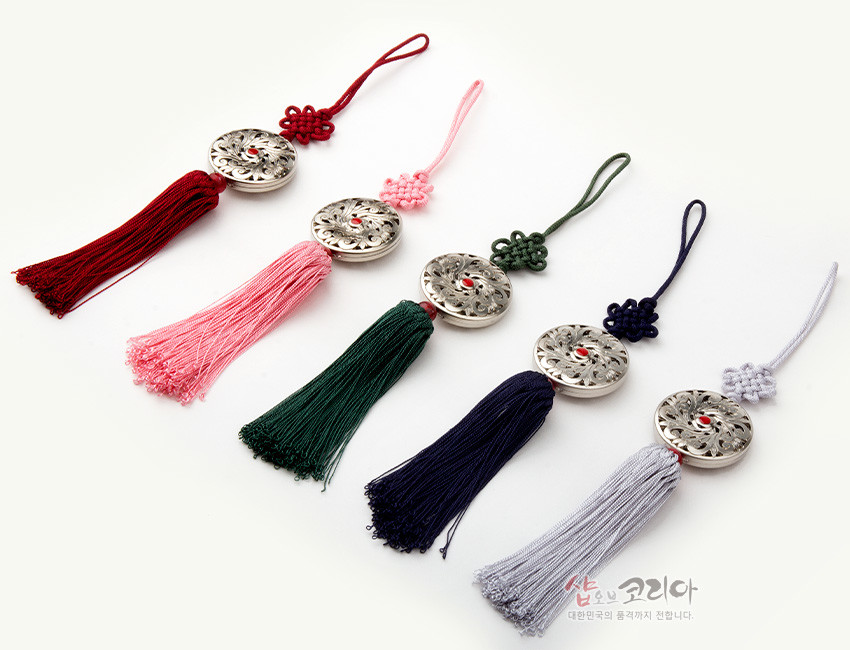 [텍스트: 샵오브코리아 대한민국의 품격까지 전합니다.] 금속제 원형 당초무늬 장식과 중앙 홍색 보석 장식, 전통 매듭과 붉은색·분홍·녹색·남색·연회색 실타슬이 조화를 이룬 작은 노리개 장식