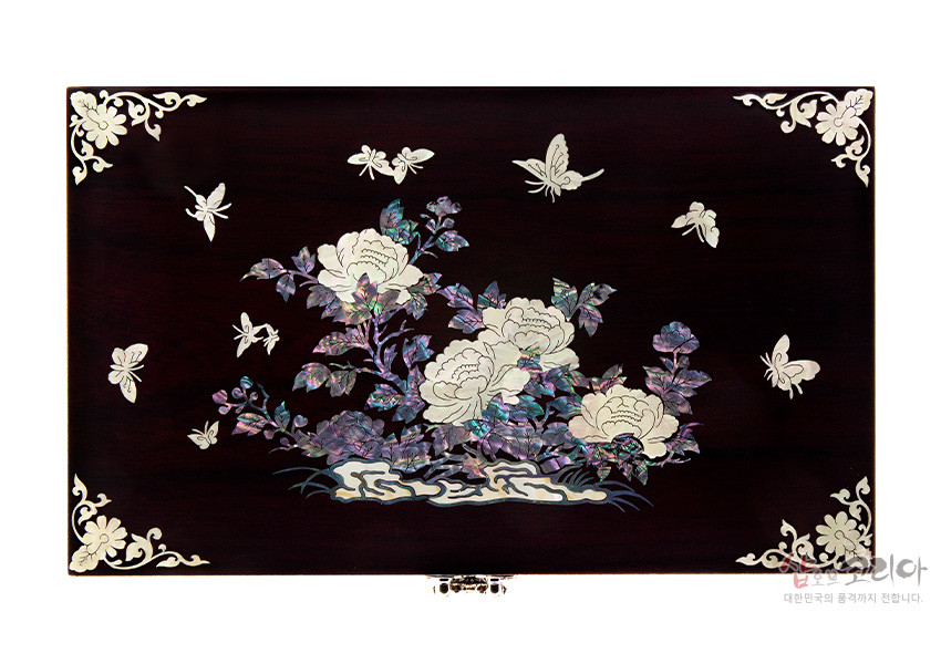 [텍스트: 샵오브코리아 대한민국의 품격까지 전합니다.] 짙은 와인빛 옻칠 목재 위 자개 상감 기법으로 표현한 목단과 나비 문양, 모서리 백색 장식 문양이 조화를 이루는 직사각형 보석함 상판 디자인