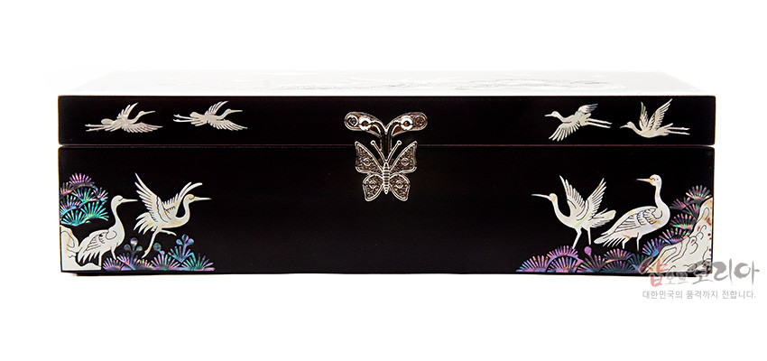 [텍스트: 샵오브코리아 대한민국의 품격까지 전합니다] 짙은 흑색 옻칠 위에 자개 상감 기법으로 소나무 숲과 학, 나비 금속 장식을 배치한 직사각형 나전칠기 보석함 정면 모습