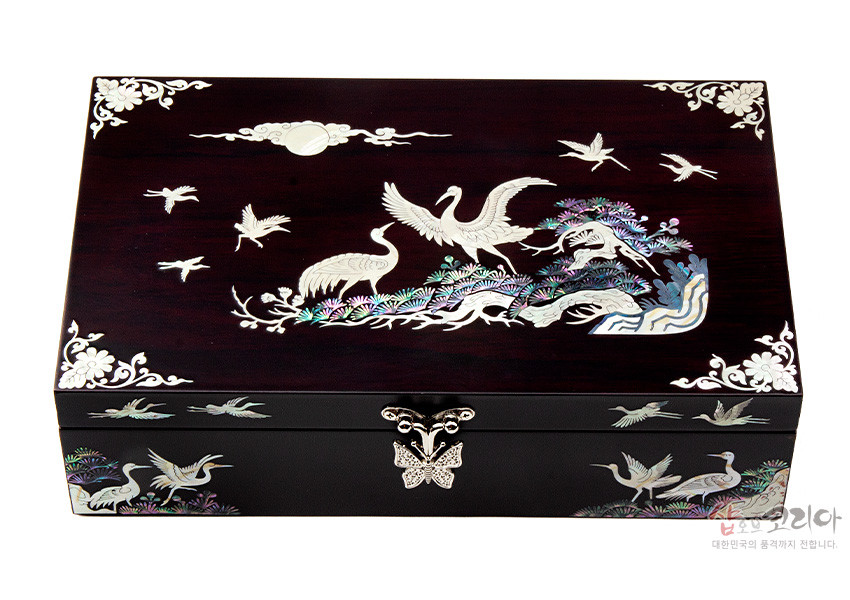 [텍스트: 샵오브코리아 대한민국의 품격까지 전합니다.] 짙은 옻칠 나무 바탕 위 자개 상감 기법으로 소나무와 학, 구름과 달 문양을 섬세하게 표현한 직사각형 나전칠기 보석함