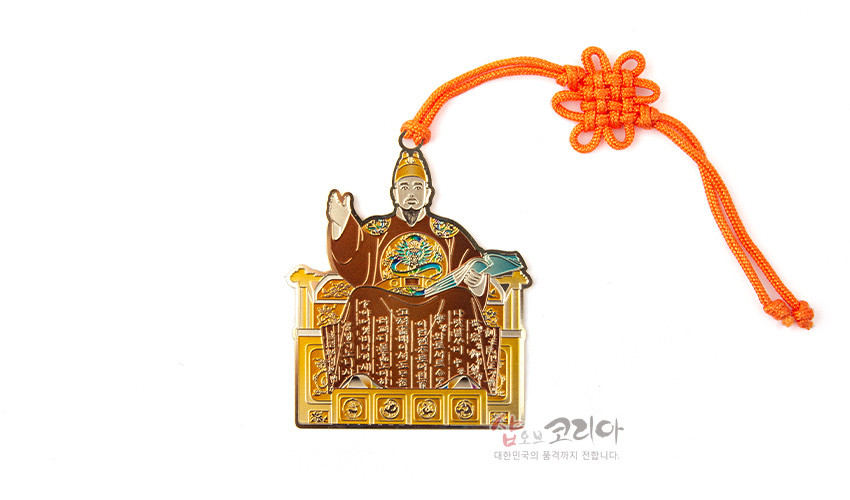 [텍스트: 샵오브코리아 대한민국의 품격까지 전합니다.] 금속 재질에 세종대왕 어좌상과 한글 문자 문양을 채색한 장식, 주황색 전통 매듭 끈이 더해진 책갈피 디자인