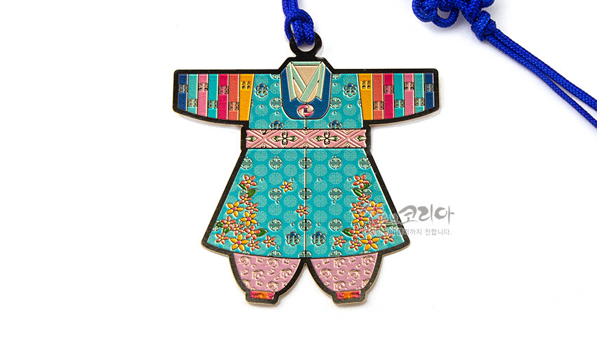[텍스트: 샵오브코리아] 금속 재질 위 채색 기법으로 표현된 아동 색동한복 모양 책갈피, 청록 바탕에 전통 문양과 꽃무늬, 분홍 띠 장식과 파란 매듭끈 조화된 디자인