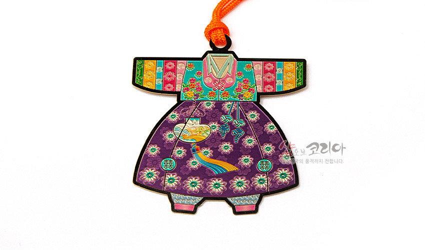 [텍스트: 샵오브코리아] 금속 재질 위 채색 기법으로 표현된 아동 색동 한복 모양 책갈피, 보라색 꽃문양 치마와 자수 장식, 다채로운 색동 소매와 주황색 매듭 끈 포인트 디자인