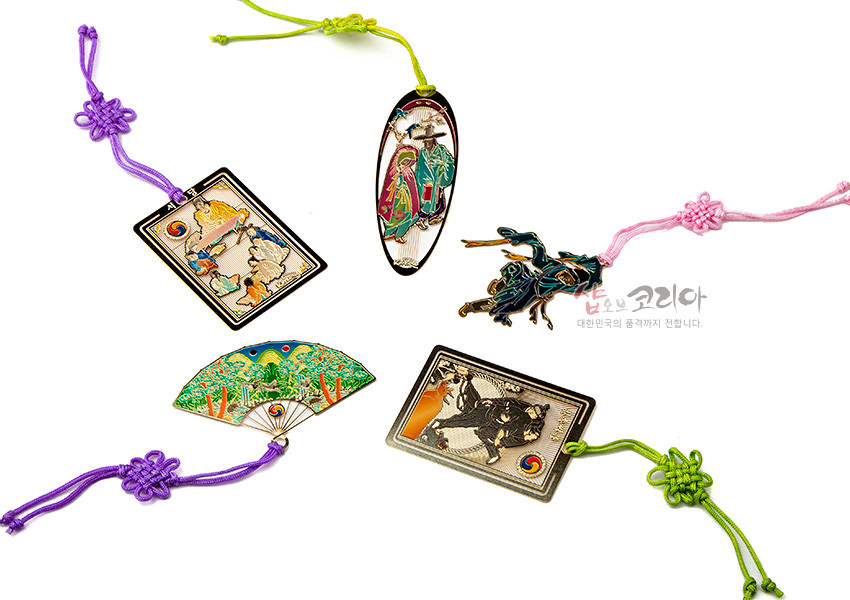 [텍스트: 샵오브코리아 대한민국의 품격까지 전합니다.] 금속 재질에 채색 기법으로 조선시대 인물·동물·풍경 문양을 표현하고 보라·연두·분홍색 전통 매듭 끈을 더한 5종 책갈피 이미지 설명