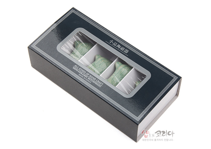 [텍스트: 小品陶磁器 / ALL KINDS OF HAND CRAFT / WITH CLASSIC PATTERNS / NEW CHINESE IN MODERN EXPRESS] 청자 재질 거북이 수저받침 5개가 투명 창을 가진 짙은 남색 종이 패키지에 정렬된 모습의 포장 이미지