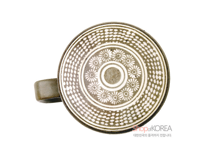 [텍스트: Shop of KOREA 대한민국의 품격까지 전합니다.] 회색 분청사기 뚜껑 위에 백색 상감 기법으로 국화문과 점열 문양을 촘촘히 둘러 장식한 머그잔 상부 모습
