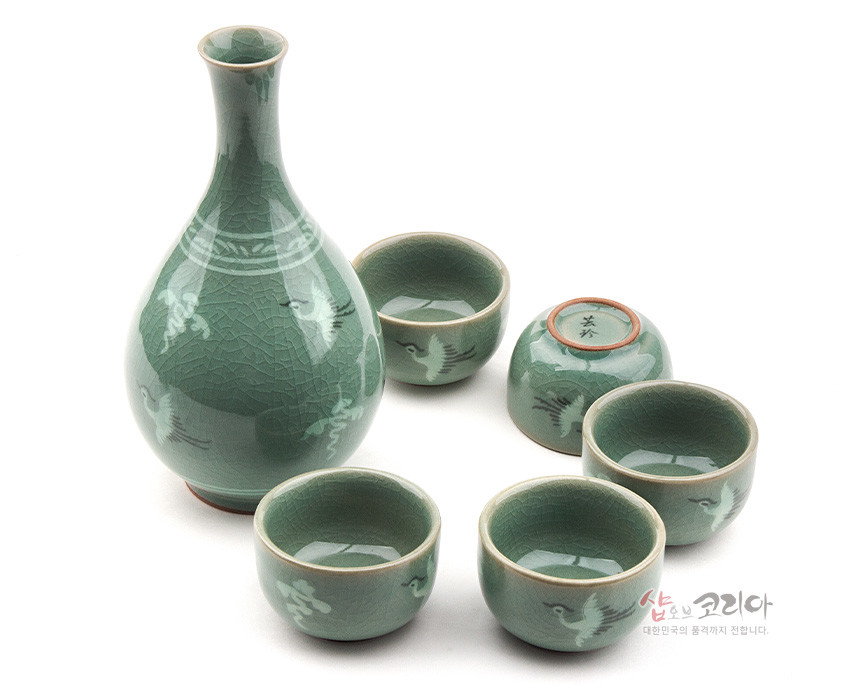 [텍스트: 샵오브코리아 대한민국의 품격까지 전합니다.] 비취색 유약과 빙렬 기법이 돋보이는 청자 주병과 술잔 세트, 학과 구름 상감 문양 장식 구성