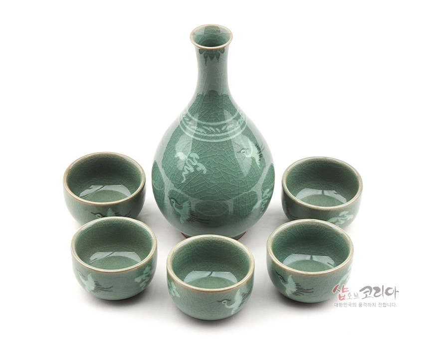 [텍스트: 샵오브코리아 대한민국의 품격까지 전합니다.] 비취색 유약과 빙렬 기법의 청자 재질, 학과 구름 상감 문양이 둘러진 주병과 술잔 세트 구성