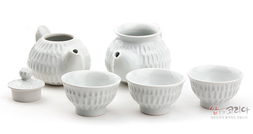 [텍스트: 샵오브코리아 대한민국의 품격까지 전합니다.] 백자 재질의 다관, 숙우, 찻잔에 규칙적인 빗살무늬 음각이 둘린 흰색 3인 다기 세트 이미지 설명