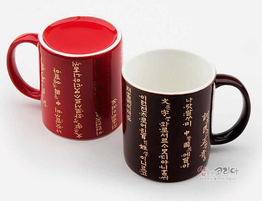 [텍스트: 나랏말ᄊ미 듕귁에 달아 文와로 서로 通 ᄮᅵ 아니할 …] 붉은색·검은색 유약 도자 머그컵에 황금빛 훈민정음 언해 서체를 세로 배치한 디자인