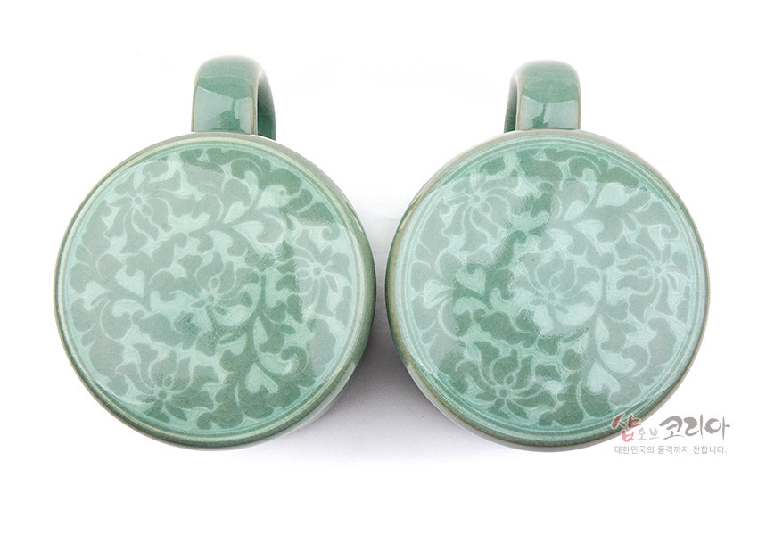 [텍스트: 샵오브코리아 대한민국의 품격까지 전합니다.] 연녹색 유약 청자 표면에 상감 기법으로 표현된 목단당초 무늬 머그컵 뚜껑 상단 디자인