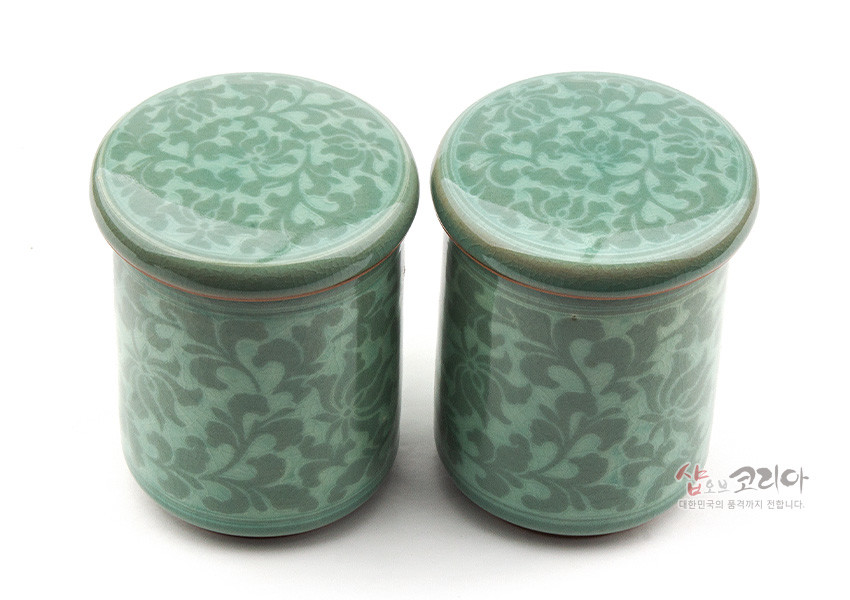 [텍스트: 샵오브코리아 대한민국의 품격까지 전합니다.] 연녹색 유약을 입힌 청자 재질, 목단당초 문양을 상감 기법으로 둘러 장식한 원통형 뚜껑 머그다기 한 쌍 이미지 설명