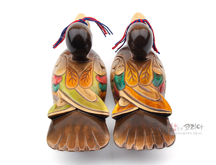 [텍스트: 샵오브코리아 대한민국의 품격까지 전합니다.] 채색 목각으로 표현한 원앙 한 쌍, 갈색 바탕에 녹색·적색·황색 깃털 문양과 홍청색 실 매듭 장식이 조화를 이룬 전통 인테리어 장식품