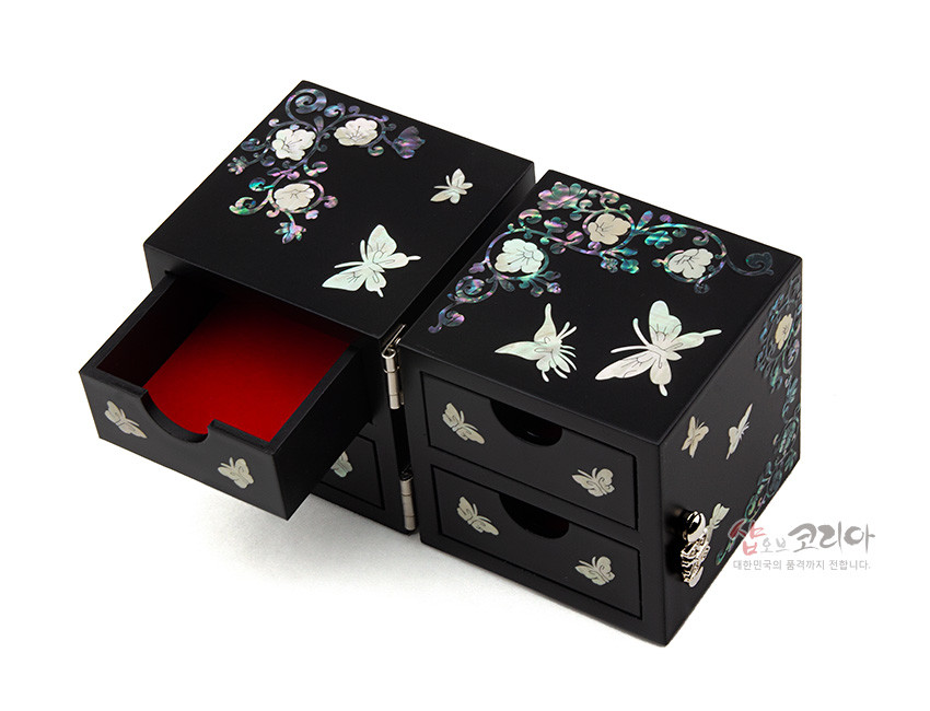 [텍스트: 샵오브코리아 대한민국의 품격까지 전합니다.] 무광 검정 옻칠 위 자개 상감으로 나비와 꽃 문양을 섬세히 장식한 금속 경첩 쌍합과 붉은 안감 서랍 구조의 공예 수납함 모습