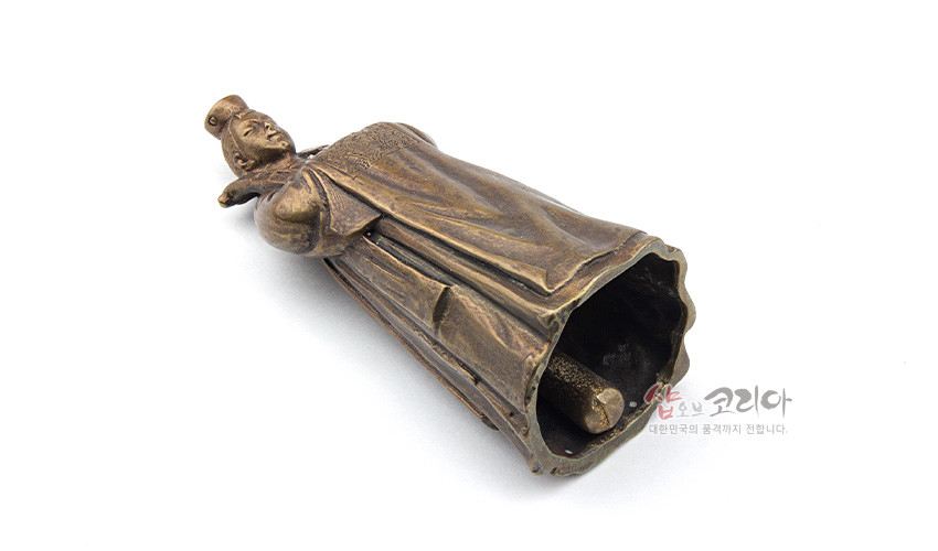 [텍스트: 샵오브코리아 대한민국의 품격까지 전합니다.] 청동빛 금속으로 제작된 전통 혼례 복식 신랑 형상의 장식종, 자연스러운 옷 주름과 내부 타공 종추가 특징인 공예품