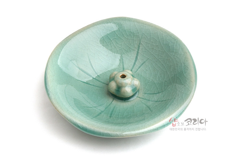 [텍스트: 샵오브코리아 대한민국의 품격까지 전합니다.] 비색 청자 유약 도자기 재질, 연잎 음각 잎맥 문양과 중앙 연꽃봉오리 형 향꽂이 장식 접시 디자인