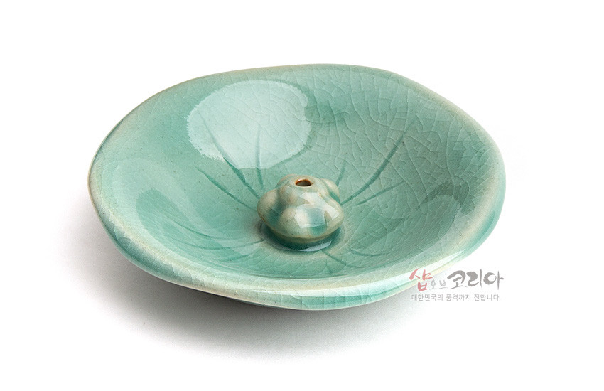 [텍스트: 샵오브코리아 대한민국의 품격까지 전합니다.] 비취색 청자 유약 도자기 향꽂이, 연잎 음각 잎맥 문양과 중앙 연꽃봉오리 형상 장식 접시형 구성