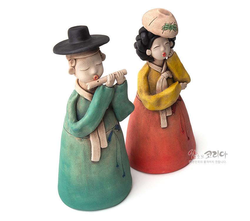 [텍스트: 샵오브코리아, 한국인의 품격까지 전합니다.] 황토를 저온 소성해 제작한 도자 인형 한쌍, 녹청·황·홍색의 그러데이션 한복 채색과 단순화된 얼굴 조형이 어우러진 전통 공예 인형 세트 이미지