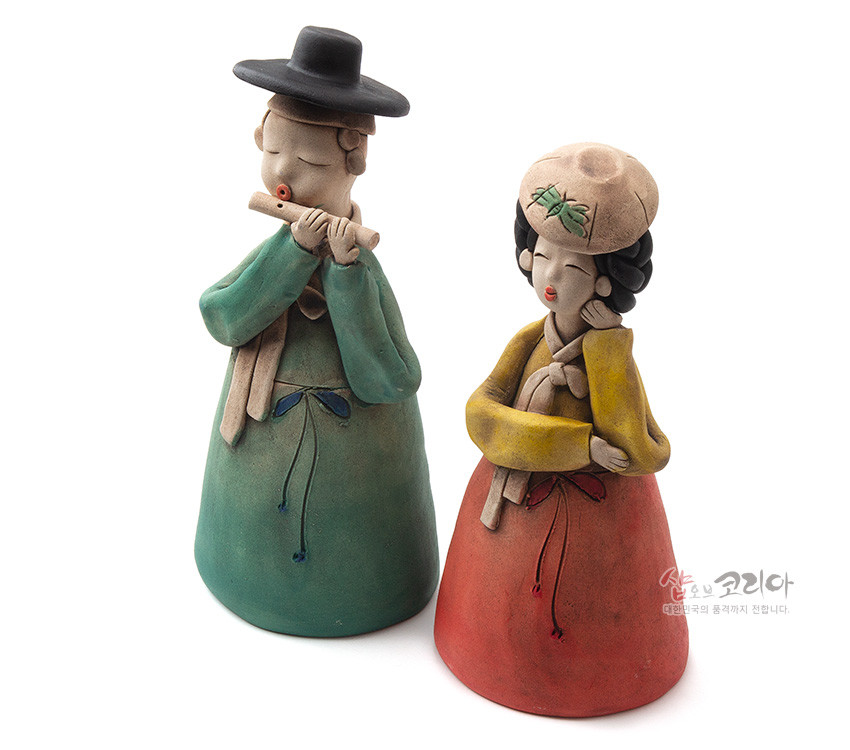 [텍스트: 샵오브코리아 대한민국의 품격까지 전합니다.] 황토를 빚어 저온 소성한 도자기 인형, 녹색·적색 한복과 노랑 저고리의 대비색, 단순화된 얼굴과 모자 자수 문양이 조화를 이루는 선비·여인 한쌍 장식품