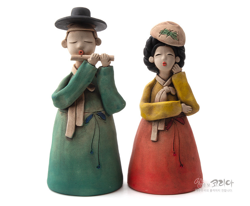 [텍스트: 샵오브코리아 대한민국의 흔적까지 전합니다.] 황토 재질로 빚어 저온 채색한 선비와 여인 도자 인형, 녹색·붉은색 대비 한복과 단순화된 얼굴, 모자 대나무 잎 문양이 특징인 공예 장식품