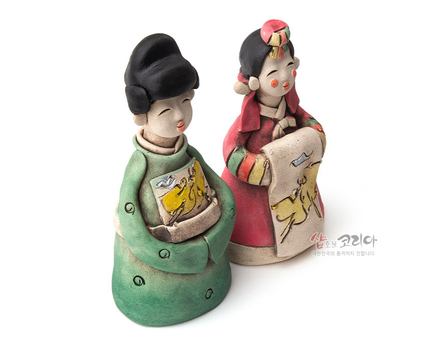[텍스트: 샵오브코리아 대한민국의 품격까지 전합니다.] 황토 소지로 빚어 구운 후 녹색·적색으로 채색한 신랑신부 도자 인형, 앞면 황색 동물 문양 패널과 한복 디테일이 돋보이는 전통 혼례 장식 인형