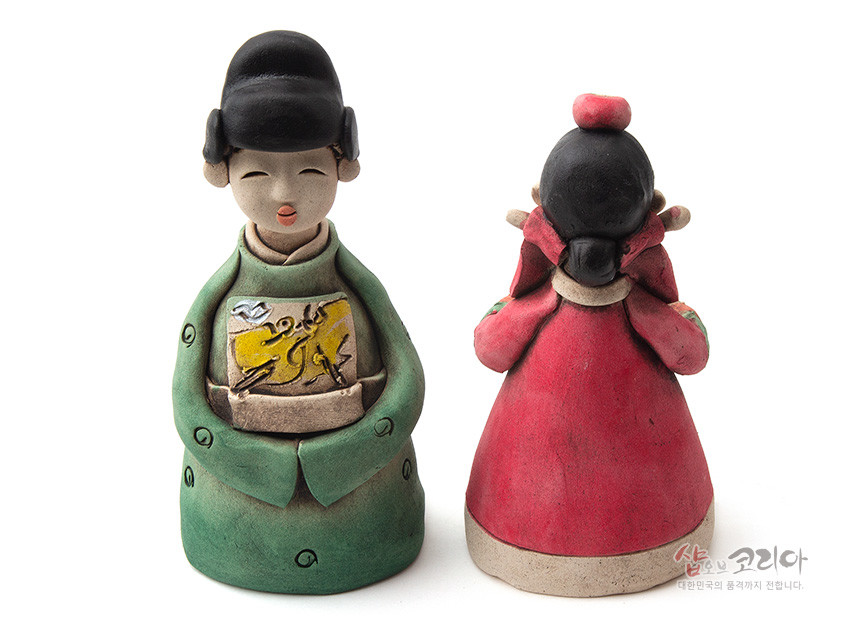 [텍스트: 샵오브코리아 대한민국의 품격까지 전합니다.] 황토를 빚어 저온 소성한 도자 인형, 녹색·홍색 한복 채색과 앞면 수묵화풍 노란 패널 문양이 돋보이는 전통 혼례 신랑신부 조형물