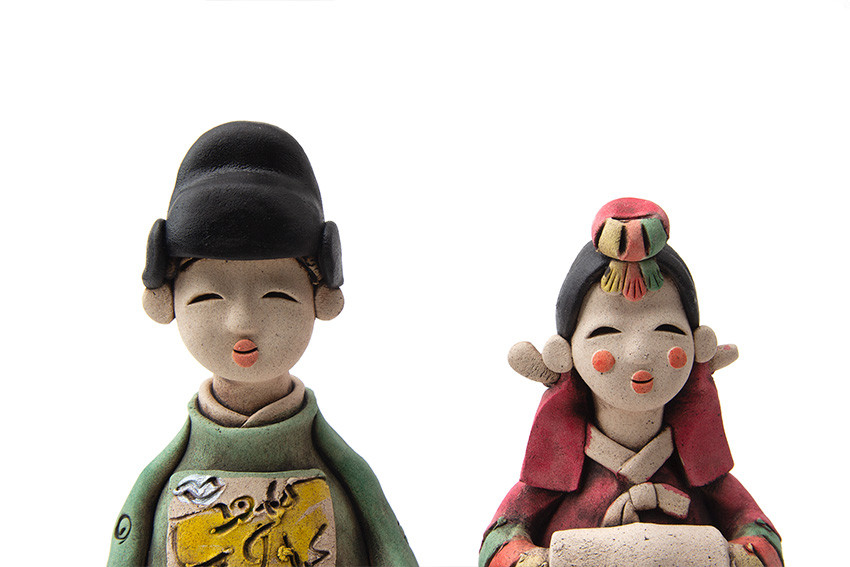 [텍스트: 없음] 황토 도자 재질로 만든 전통 혼례 신랑신부 인형, 녹색·홍색 한복과 삼색 노리개, 상의 황색 문양 장식이 돋보이는 디자인