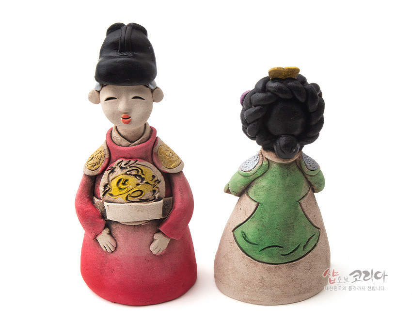 [텍스트: 샵오브코리아 대한민국의 품격까지 전합니다.] 붉은 곤룡포와 용문양, 녹색 당의와 뒤꽂이 머리장식이 돋보이는 채색 황토 왕과 왕비 도자 인형 장식