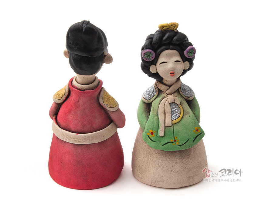 [텍스트: 샵오브코리아 대한민국의 품격까지 전합니다.] 붉은 곤룡포와 녹색 저고리 한복을 입은 황토 도자기 왕과 왕비 인형, 어깨 장식과 꽃문양 채색이 돋보이는 전통 조형물