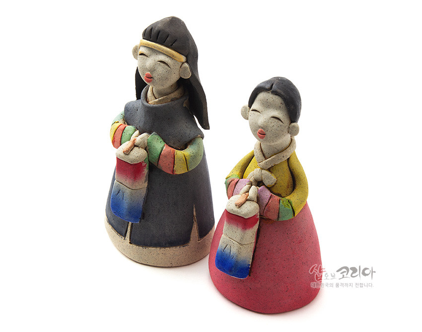 [텍스트: 샵오브코리아 대한민국의 품격까지 전합니다.] 황토 느낌의 채색 도자 재질 한복 남녀 인형, 색동 소매와 붉은·파란 청사초롱을 든 단순화된 조형미의 전통 장식 인형 모습