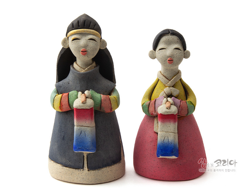 [텍스트: 샵오브코리아 대한민국의 품격까지 전합니다.] 황토 질감의 도자 기법으로 제작된 남녀 한복 인형, 색동 소매와 붉은·파란 그라데이션 청사초롱을 든 단순화된 전통 조형미 강조 이미지
