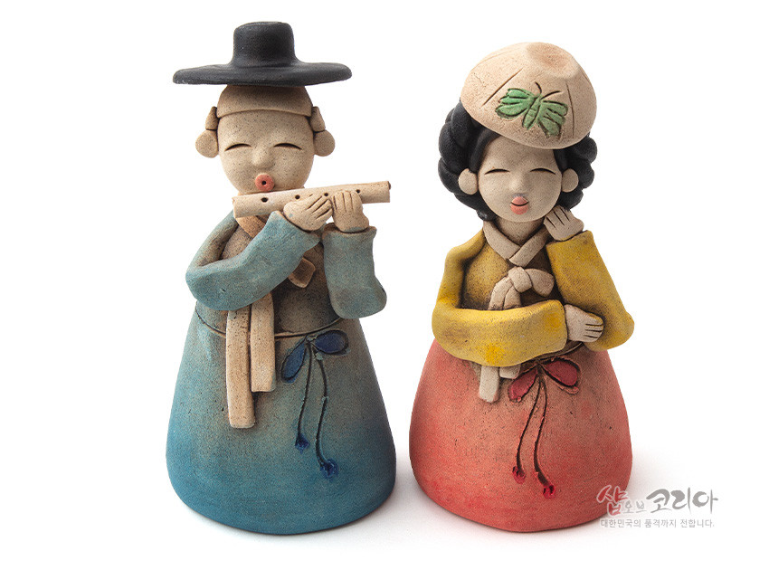 [텍스트: 샵오브코리아 대한민국의 품격까지 전합니다] 황토 도자 재질로 빚은 선비와 여인 한복 인형, 파스텔톤 청·홍·황 색감과 나비 문양 모자 장식이 어우러진 전통풍속 조형 작품