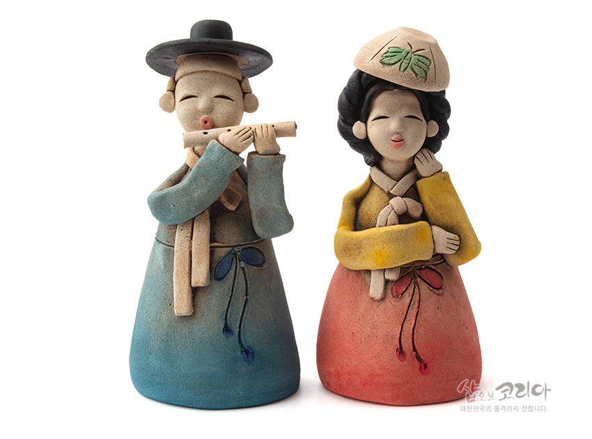 [텍스트: 샵오브코리아 대한민국의 품격까지 전합니다.] 황토 재질 도자기 인형, 파스텔톤 청·홍·황색 한복 채색과 나비 문양 모자, 단순화된 얼굴 조형의 전통 연인 형상