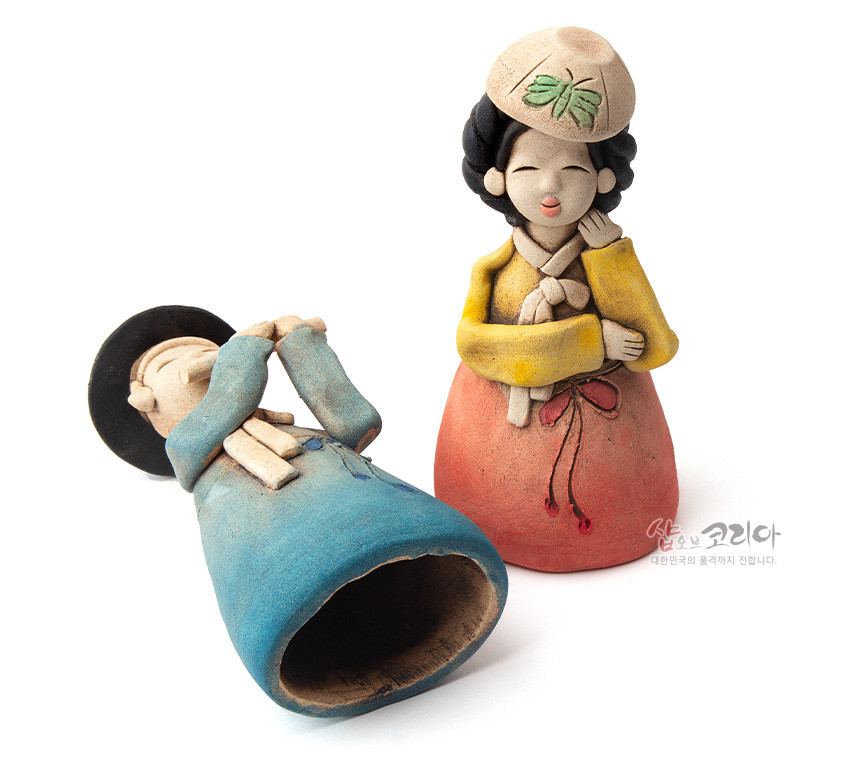 [텍스트: 샵오브코리아 대한민국의 품격까지 전합니다.] 황토로 빚은 선비와 여인 한복 인형, 파스텔톤 청·황·홍색 채색과 나비 문양 모자 장식, 소박한 얼굴 조형의 도자 공예 장식품