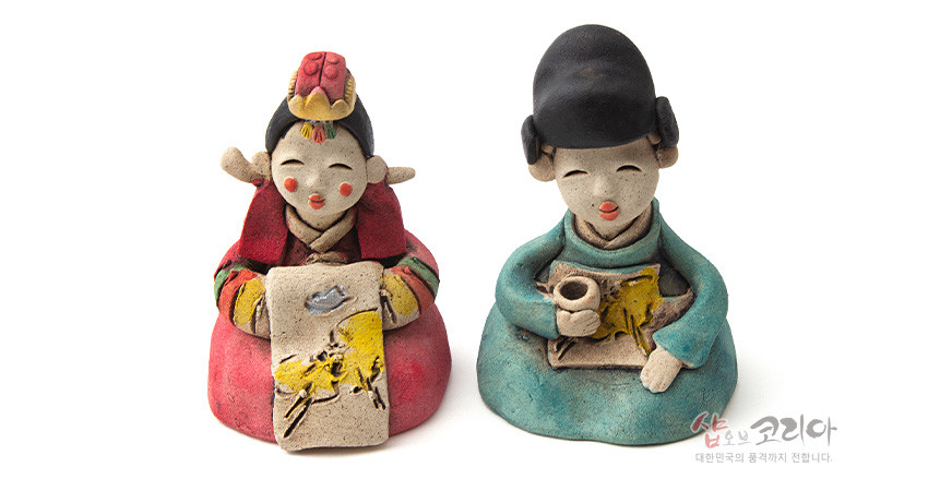[텍스트: 샵오브코리아 대한민국의 품격까지 전합니다.] 황토 재질 도자기 기법의 전통 혼례 신랑신부 인형, 붉은색·청록색 한복과 노란 수묵화풍 회화문 장식이 특징인 좌식 형상 작품