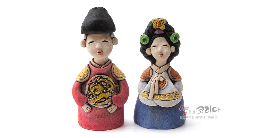 [텍스트: 샵오브코리아 대한민국의 품격까지 전합니다.] 황토 느낌 도자기로 빚은 왕과 왕비 인형 한 쌍, 붉은 곤룡포와 청색 치마저고리, 금색 용 문양과 화려한 머리장식이 돋보이는 전통 한복 인형 조형